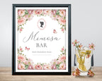 Framed 'Mimosa Bar' sign with blush pink floral design next a glass of mimosa on a wooden surface.