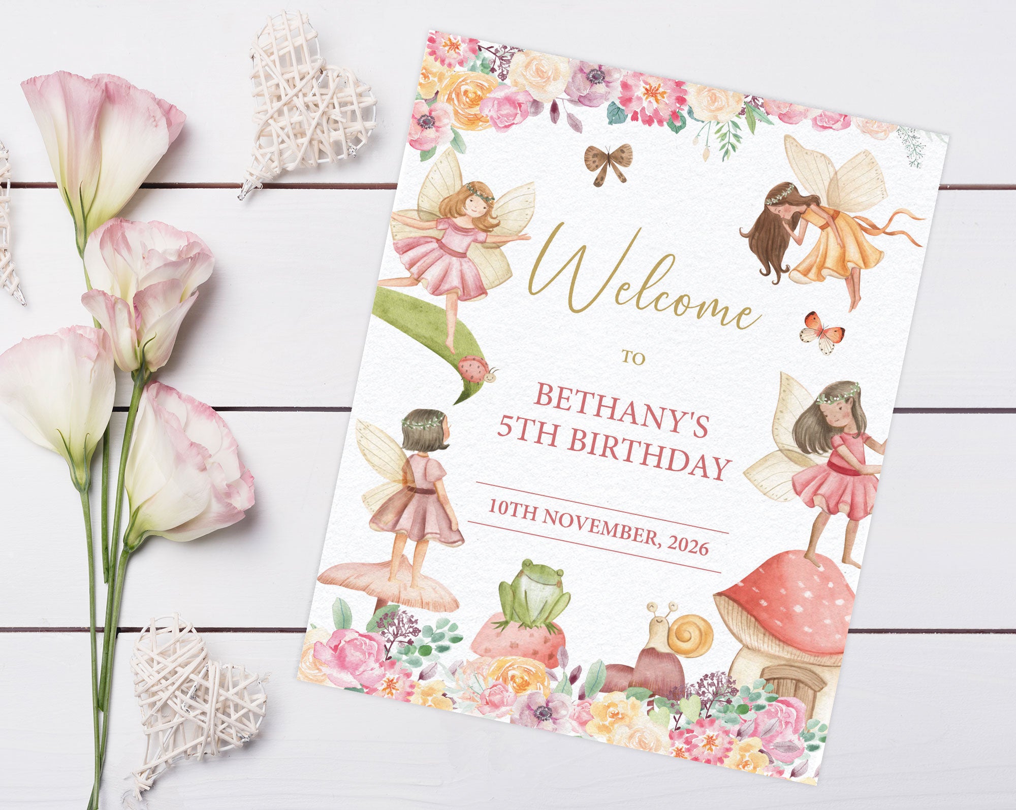 a pretty 8 x 10 fairy garden tea party welcome sign laying on a grey wooden surface next to some lilly's and decorative hearts