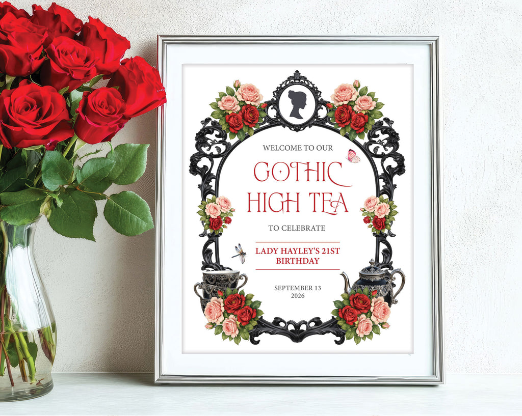 red and black gothic high small welcome sign in a silver frame leaning up against a white wall next to some red roses