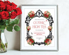 red and black gothic high small welcome sign in a silver frame leaning up against a white wall next to some red roses