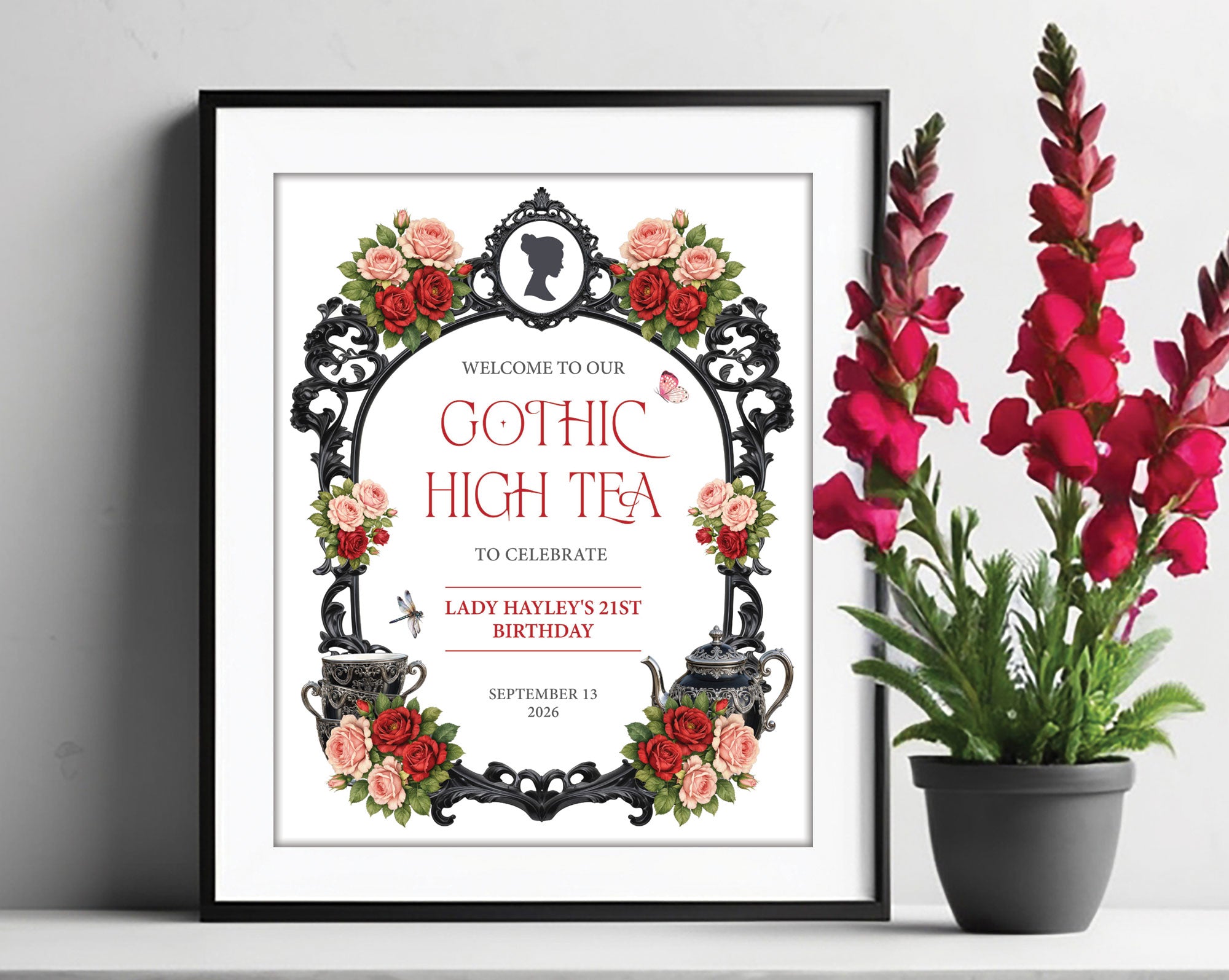 a black frame containing an 8 x 10 gothic high tea welcome sign with regency style cameo, teapot and tea cups next to some red flowers in a pot