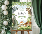A1 dinosaur and volcano party welcome sign on an easeal in front of a window with green curtains and some greenery with white balloons