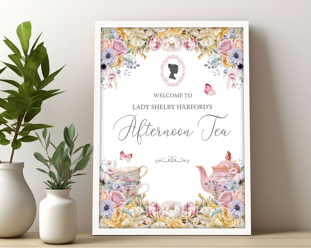 pastel welcome sign for an afternoon tea event with floral and teapot designs, in a frame, leaning up against a wall next to plants.
