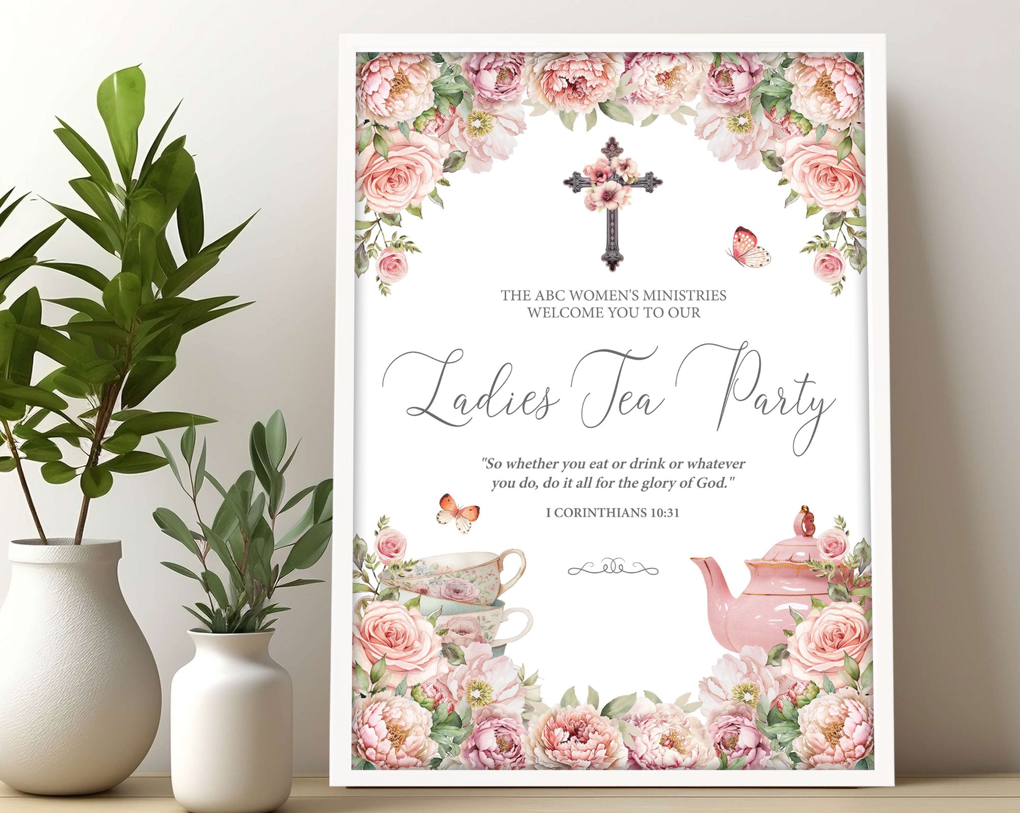 A3 Church Ladies Tea Welcome Sign in a white frame with blush pink flowers, Christian Cross and Teapot leaning up against a wall next to some greenery in vases