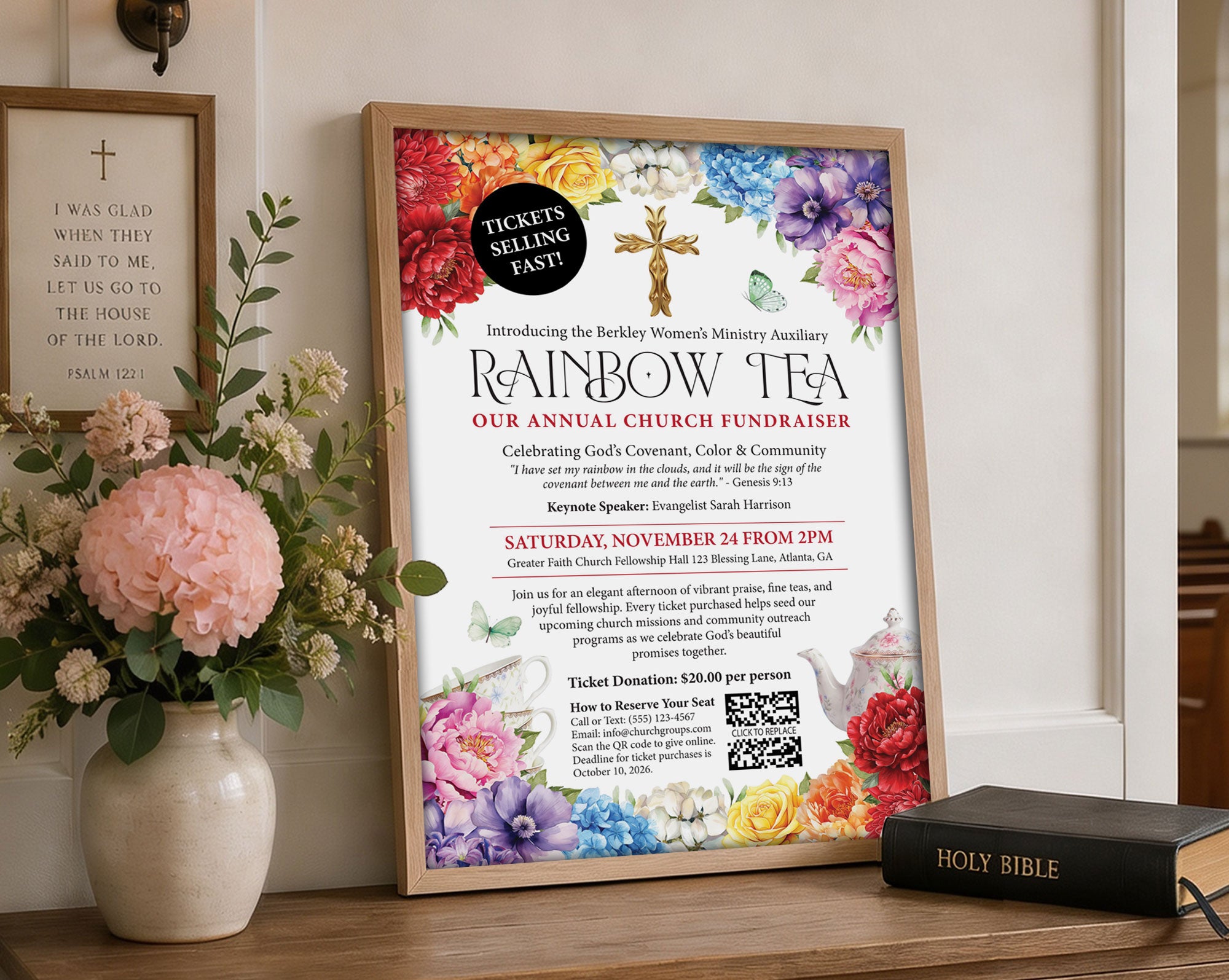 an A3 fundraising poster with QR code for a Church Rainbow Tea, in a wooden frame leaning up against a wall next to some flowers in a vase and a religious sign on the wall