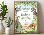 A3 kid's dinosaur party welcome sign with various dinosaurs, volcano and prehistoric forest graphics, in a wooden frame, leaning on a beige wall next to two white vases with greenery