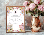 Decorative sign for a high tea event with floral design and a copper vase with pink roses.