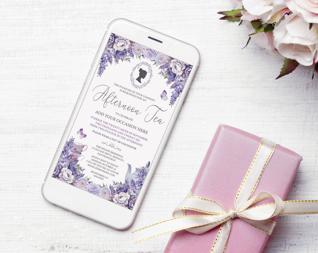 A white smartphone lying on a white wood surface displays a purple floral invitation design for an afternoon tea. A pink gift box tied with a cream ribbon sits beside it, with pale pink flowers in the top-right corner.