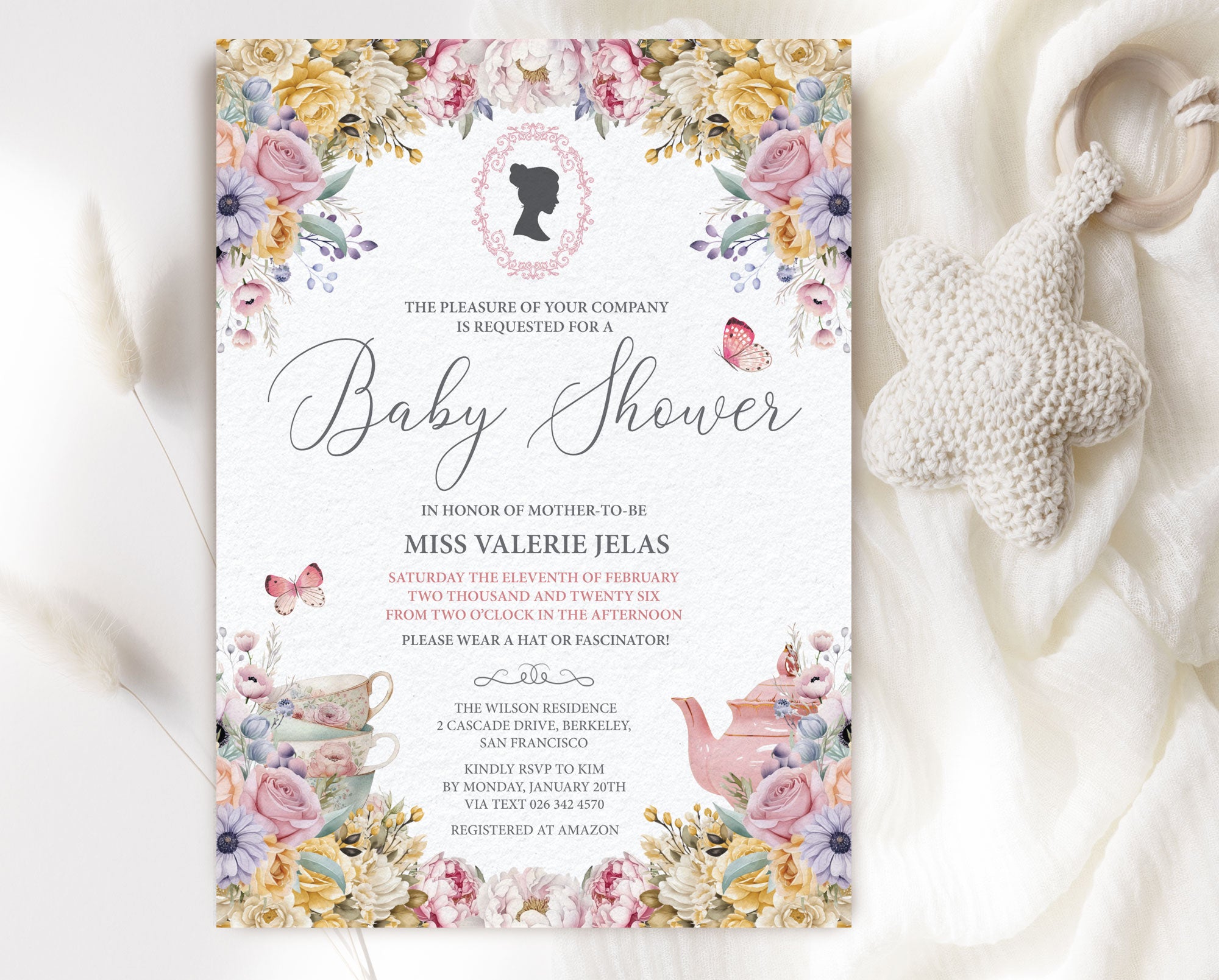 regency baby shower invitation with cameo, teapot and pastel flowers laying on a white cloth with a knitted baby pacifier next to it