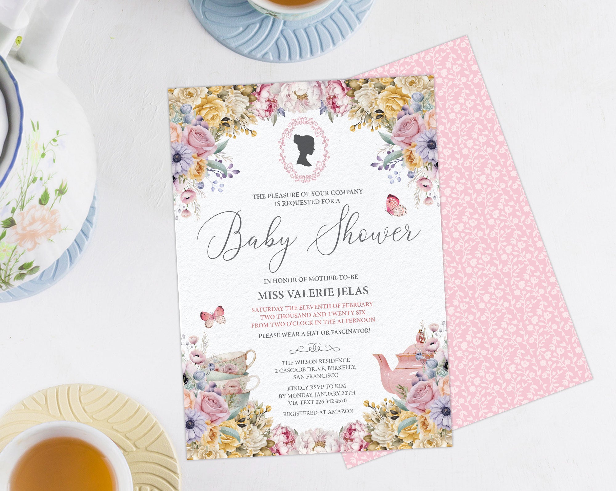 a pastel flower baby shower invitation showing the front and the pink pattern back, laying on a white background next to a pastel tea service