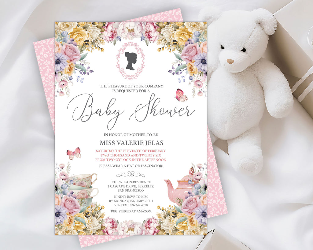 an elegant pastel baby shower tea regency style invitation laying on the pink pattern back of the invite, on a white cloth with a white teddy bear and a wrapped gift