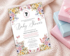 a pastel baby shower invitation with cameo and flowers on a cream baby blanket next to some pink and blue wrapped gifts