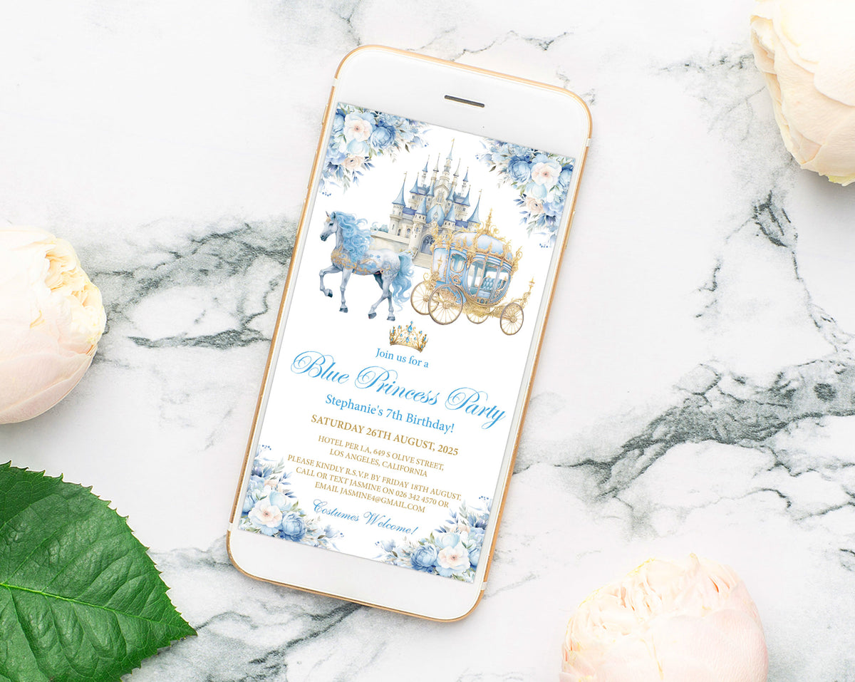 A smartphone lying on a white marble surface with pale flowers and a green leaf around it, displaying a blue and white princess party invitation design with a carriage and castle illustration.