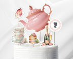 Decorative cake toppers with pink teapot, cups, cake, and champagne bottle on a white background