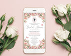 a pretty blush pink flower invitation showing on the screen of a white mobile phone laying on a pink background with white roses next to it