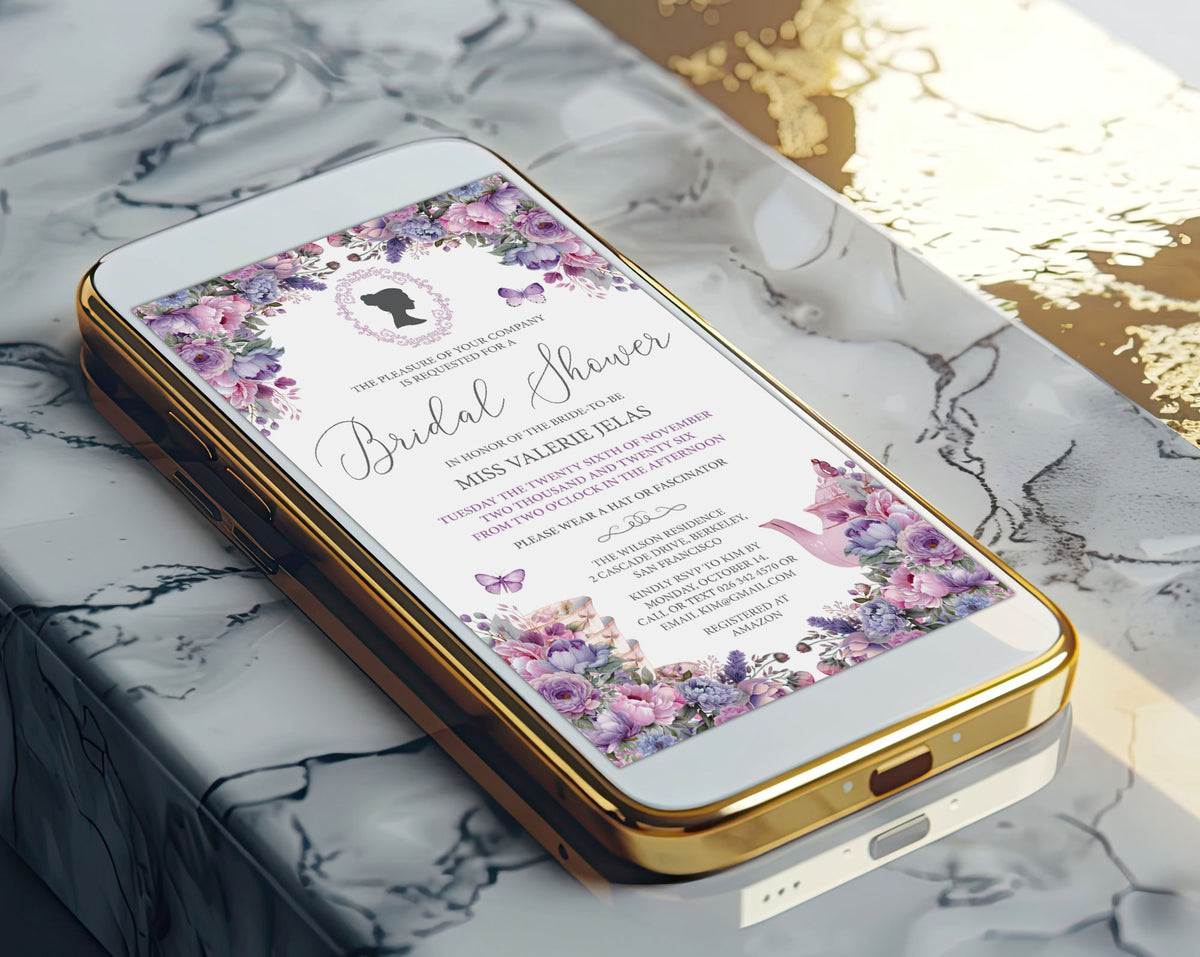 A gold-framed smartphone lying on a white marble surface, displaying a bridal shower invitation design with pink & purple floral borders, pink script text, and butterfly motifs.