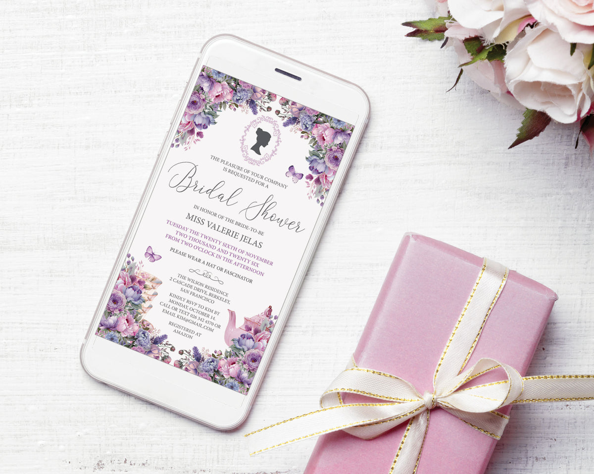 A bridal shower invitation displayed on a smartphone screen, styled in a flat lay with a pink gift box tied with a cream ribbon and white flowers on a white wooden surface.