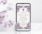 A smartphone centered on a white surface, displaying a floral bridal shower invitation design with purple and pink blossoms and black text. The phone is framed against a white background with decorative purple flowers and leaves along the left side.
