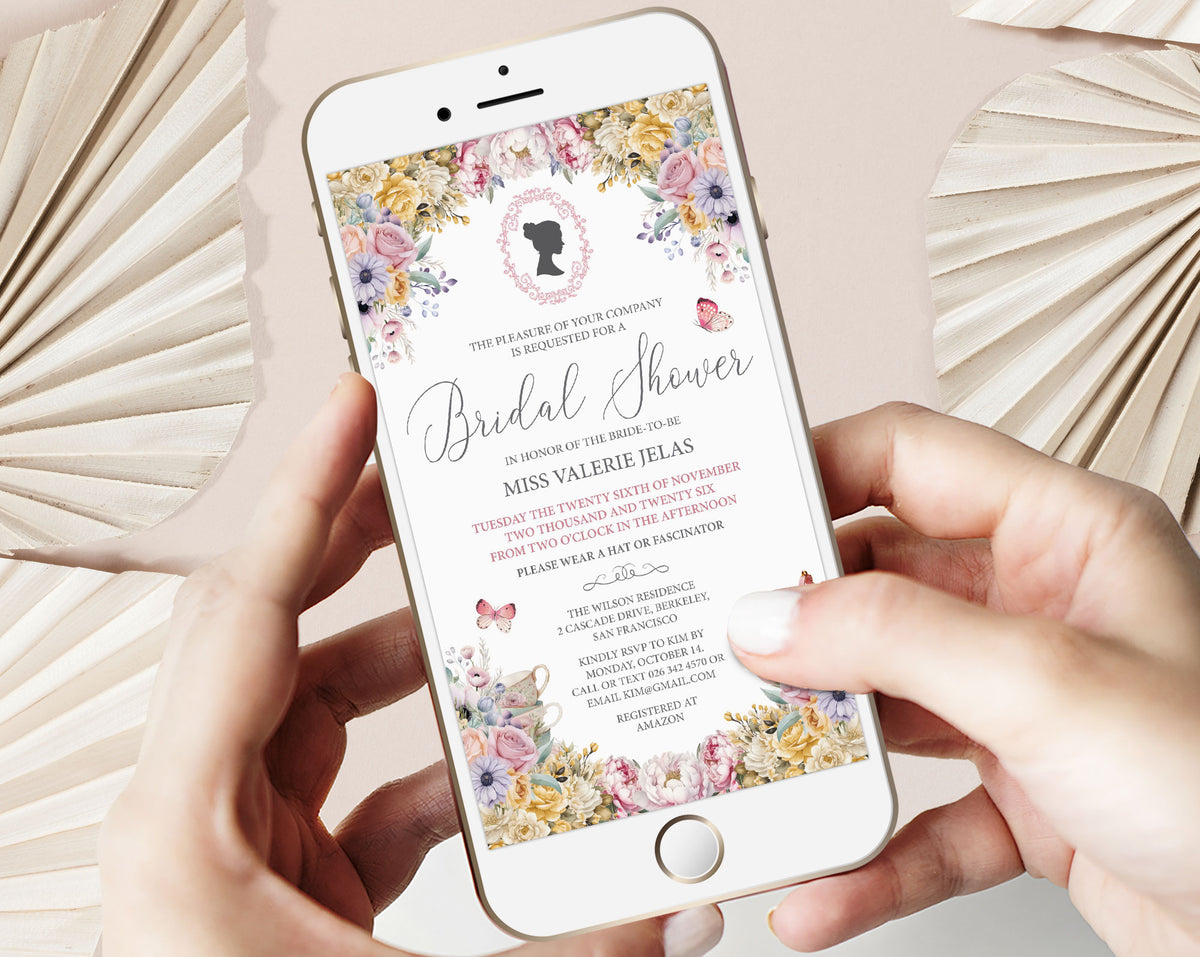 two hands holding a mobile phone with a pastel flower regency style bridal shower invitation showing on the screen, beige dried leaves in the background