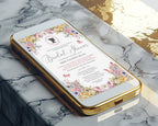 A gold-framed smartphone lying diagonally on a white and gray marble surface, displaying a bridal shower invitation design with pastel florals, regency cameo and butterflies