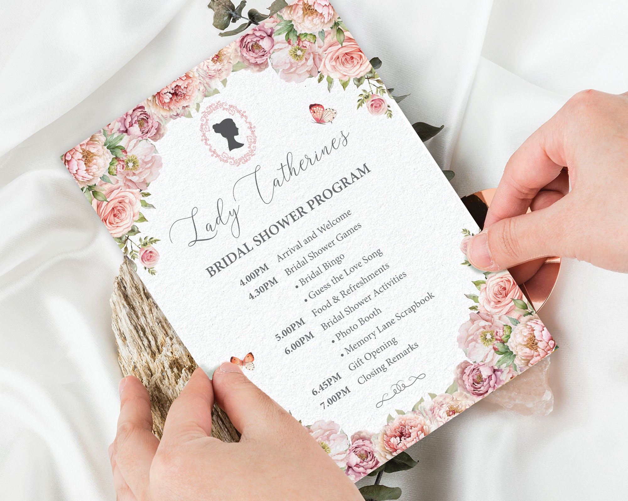 Pink Bridal shower program with floral design held by hands on a white fabric background
