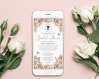 A smartphone lying on a soft pink surface, displaying a regency style blush pink floral bridal shower invitation design. White roses and rose buds are arranged around the phone, creating a styled flat-lay composition.