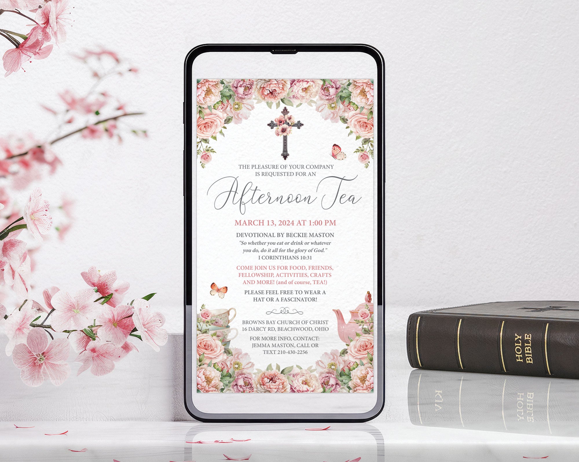 Phone displaying a blush pink church ladies afternoon tea invitation with floral cross on a white surface with flowers and bible