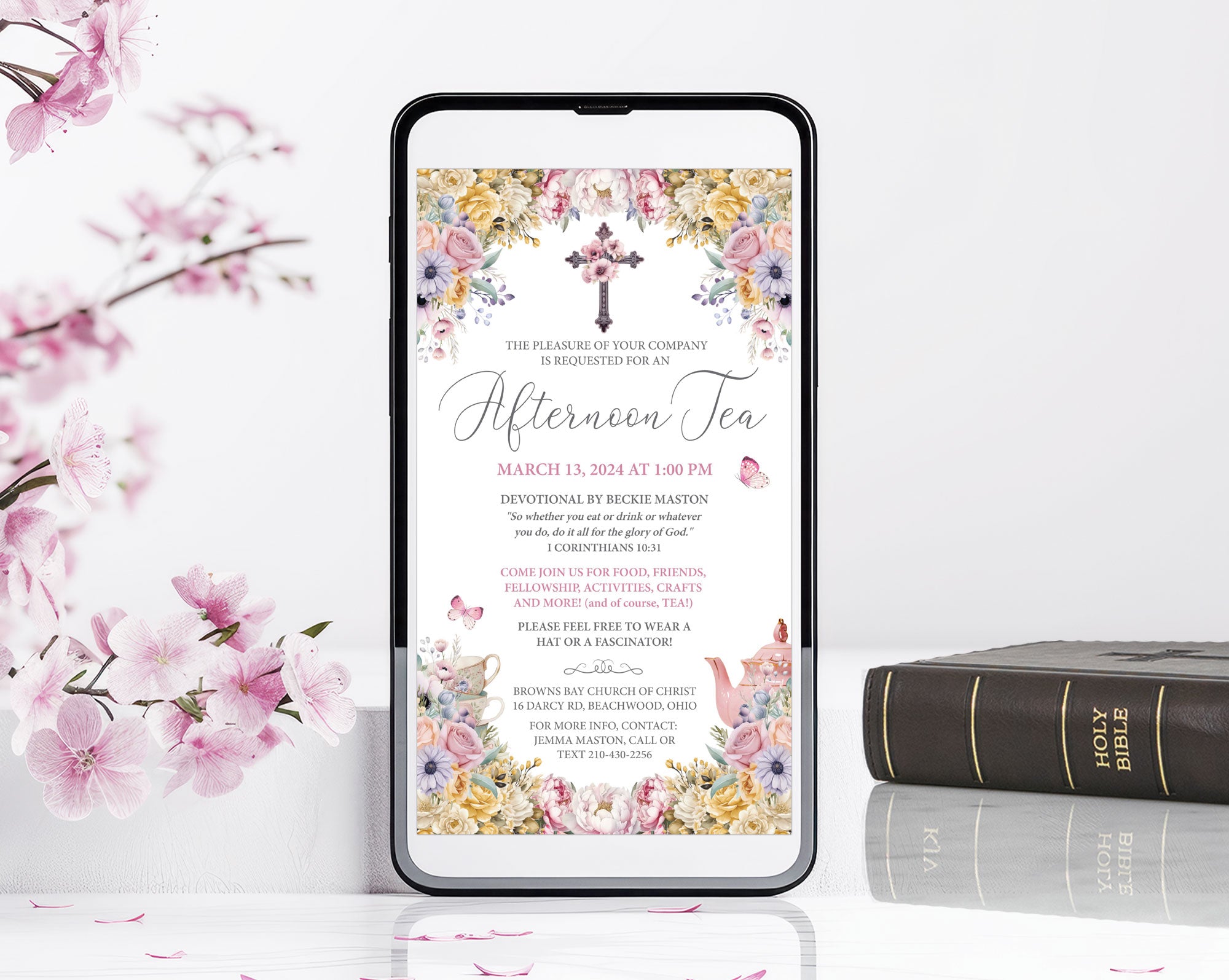 Phone displaying an religious afternoon tea invitation with floral design, surrounded by pink flowers and bible