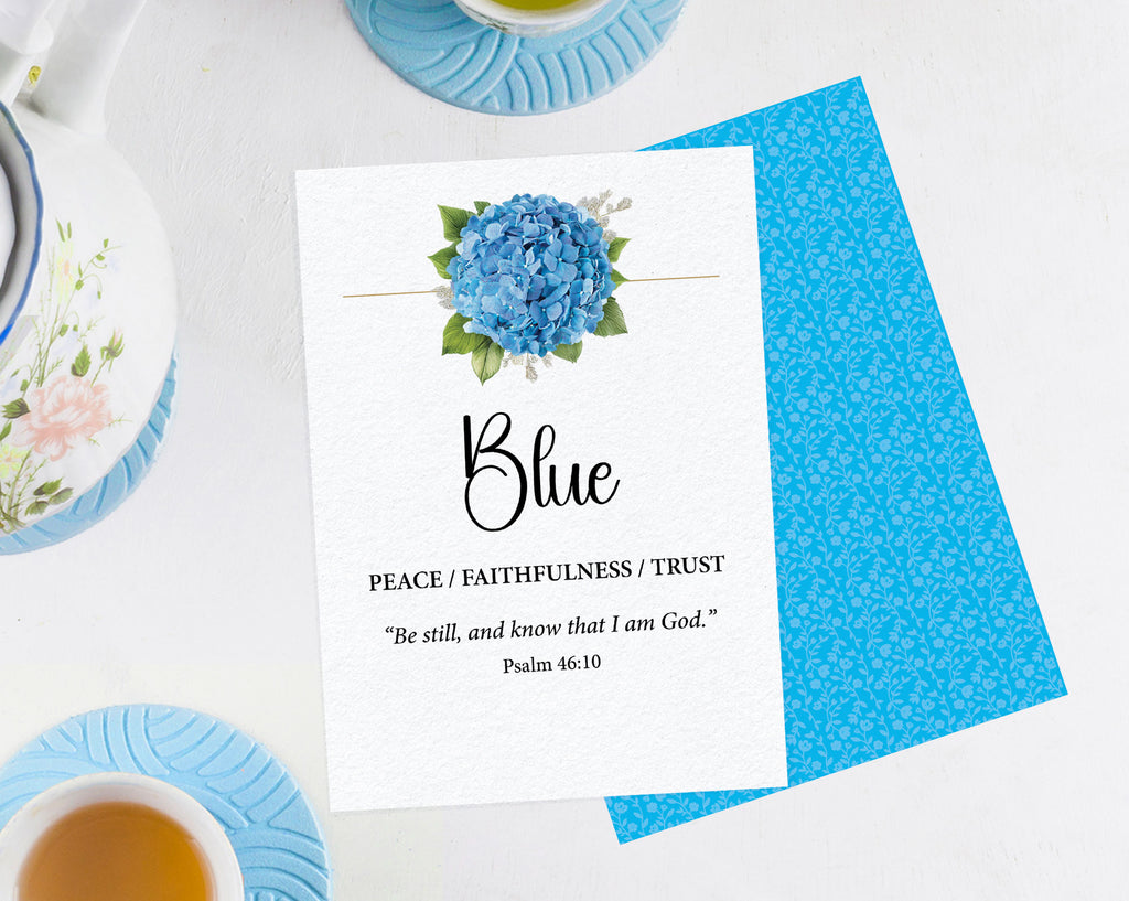 two 5 x 7 blue table cards with blue flower and scripture, laying on a white background, the 2nd card shows the blue pattern back and are surrounded by a tea set