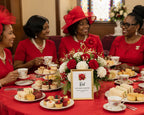 african american black ladies all dressed in bright red, sitting at a bright red Rainbow Tea table set with tea food and tea cups, with a gold framed table card with red flower and scripture