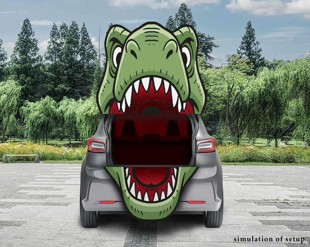A gray hatchback car shown from the rear with its trunk open, featuring a large green cartoon dinosaur mouth graphic covering the trunk opening. The scene is set outdoors on a paved area with trees and grass in the background.