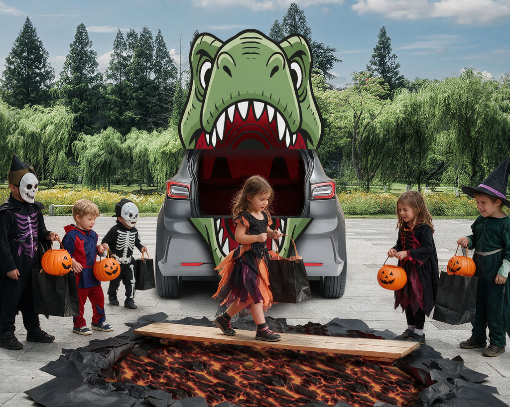 A children's Halloween scene with several kids in costumes standing around a large green dinosaur cartoon printed on the open trunk of a gray car, outdoors on a paved area with trees and bushes in the background. A fiery pit prop is in the foreground.