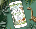 a white mobile phone with a dinosaur party invitation showing on the screen, laying on a green background with a toy dinosaur and some green leaves