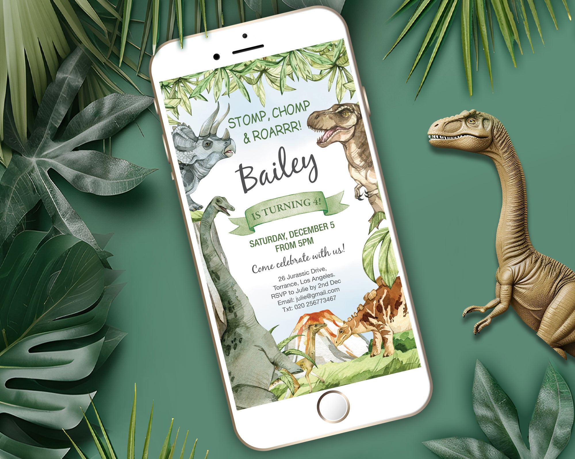 a white mobile phone with a dinosaur party invitation showing on the screen, laying on a green background with a toy dinosaur and some green leaves