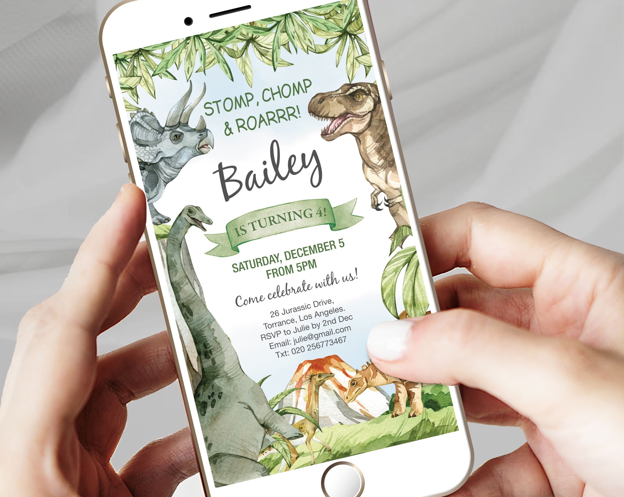 two hands holding a white mobile phone with a kids dinosaur party invitation showing on the screen with a grey background