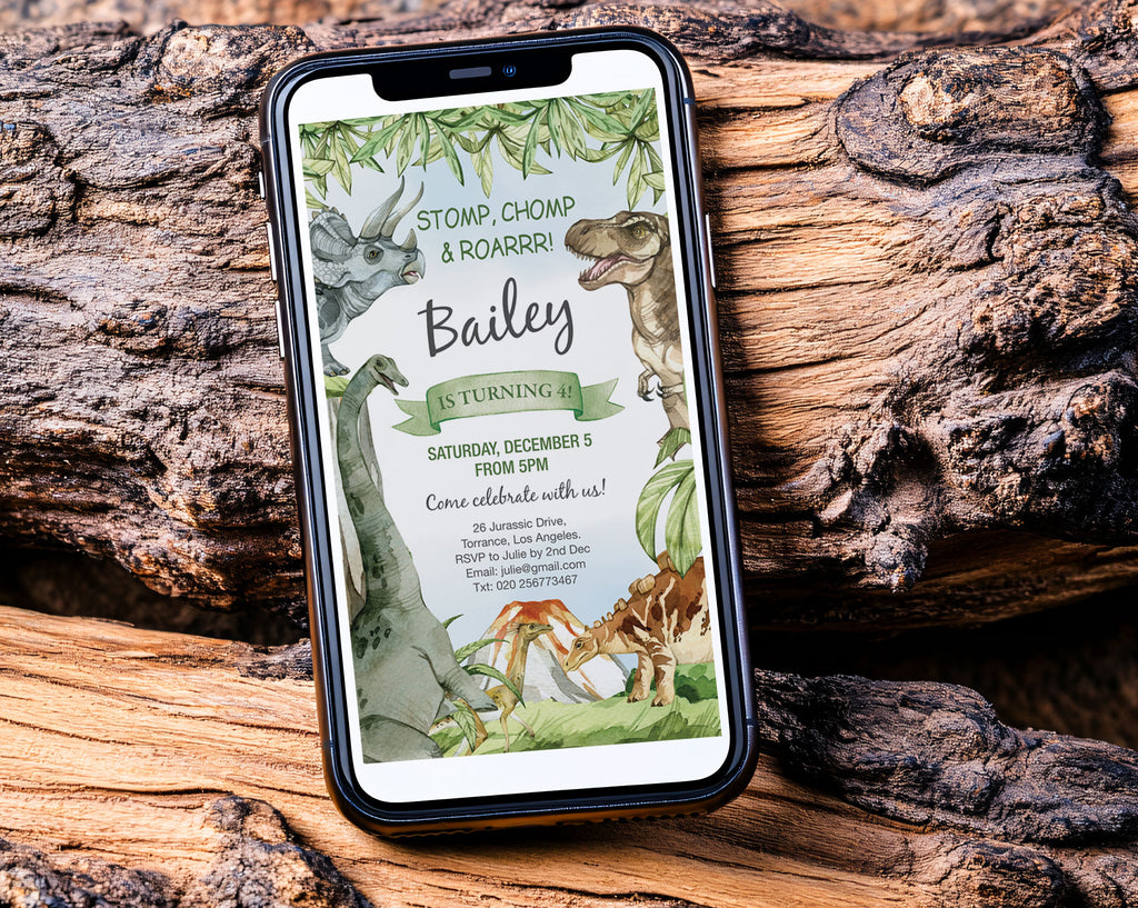 a black mobile phone with a dinosaur invitation showing on the screen leaning up against two old fallen wooden trees