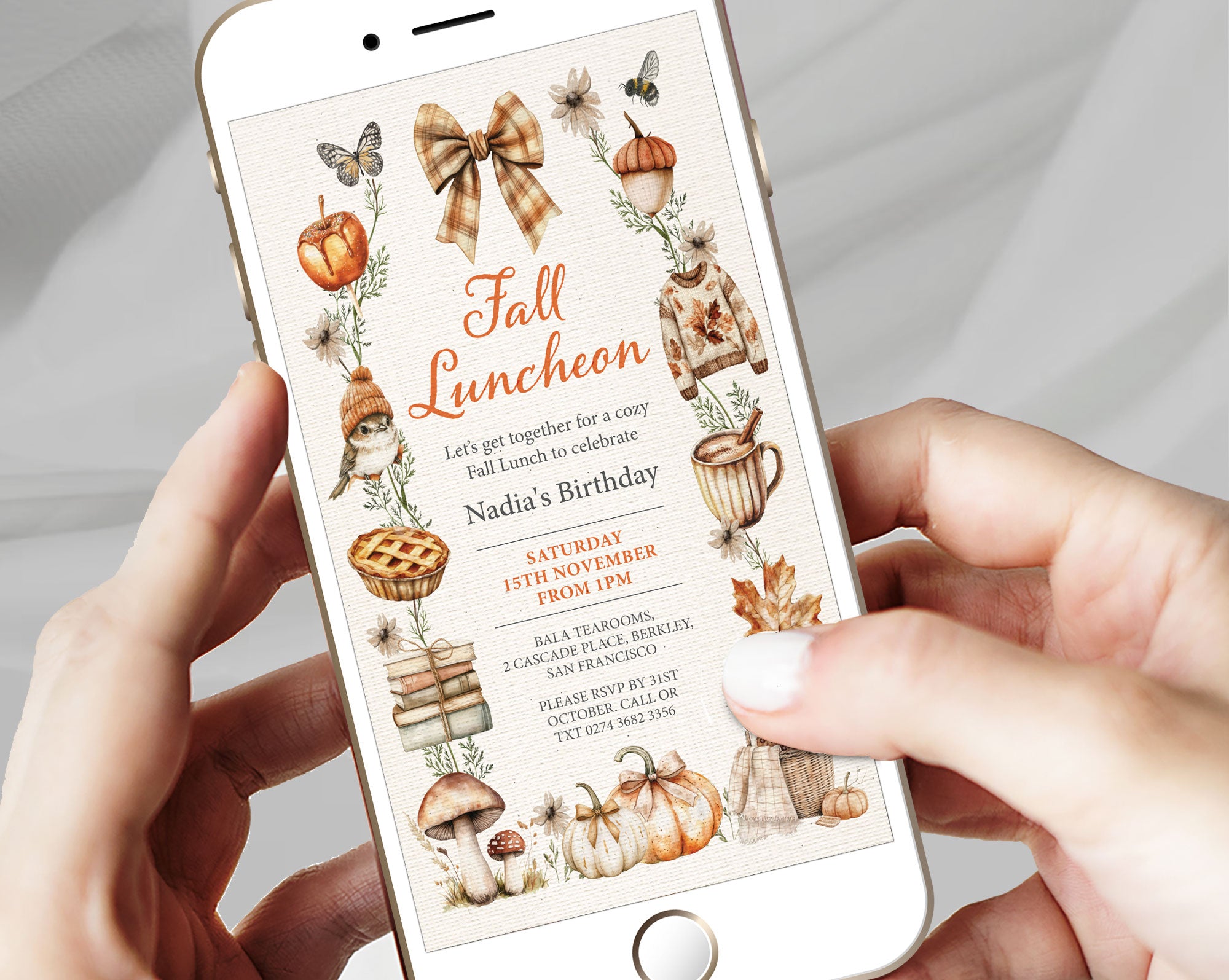 A person holding a white smartphone that displays a fall-themed birthday invitation design with autumn illustrations, including pumpkins, leaves, a plaid bow, and a bird.