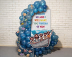 A decorative Noah's Ark themed party backdrop featuring a large white sign with the biblical quote 'FOLLOW ME AND I WILL MAKE YOU FISHERS OF MEN' and cartoon illustrations of Jesus and the children in a boat, surrounded by blue balloons, fishing net, and sea life decorations against a white brick wall.