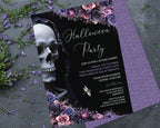 A gothic-themed Halloween party invitation card with a black background, white script text, a large white skull illustration, and purple floral borders, styled on a gray surface with scattered purple flowers and greenery.