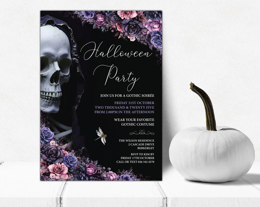 A gothic-themed Halloween party invitation card displayed on a white surface next to a white decorative pumpkin. The invitation features a black background with a large white skull, purple and pink floral borders, and white script text reading 'Halloween Party'.