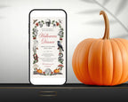 A smartphone displaying a Halloween dinner invitation design stands on a dark surface next to a large orange pumpkin. The invitation features a vintage-style floral border with a skull, bats, acorns, and the words 'Halloween Dinner' in red script.
