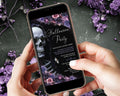 A person holds a smartphone displaying a gothic Halloween party invitation design with a skull, skeleton, and purple floral artwork. The phone is shown over a dark textured surface decorated with purple flowers.
