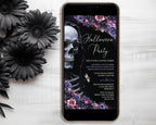 A smartphone displaying a gothic Halloween party invitation with a skull, flowers, and elegant text, placed on a white wood surface next to black daisy flowers.