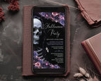 A smartphone lying on a brown leather folio, displaying a Halloween party invitation design with a skull, flowers, and gothic text. The scene is styled on a dark textured surface with dried flowers, a book, and a leather accessory nearby.