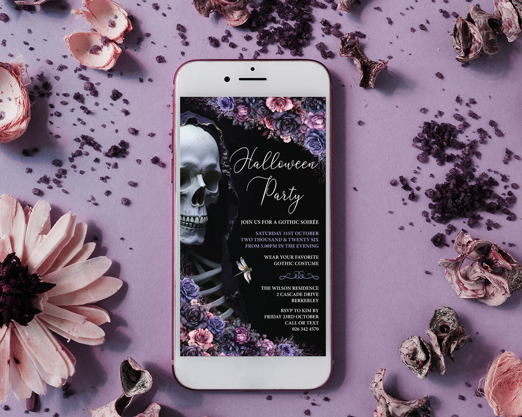 A white smartphone lying on a lavender surface, displaying a gothic Halloween party invitation design with a skull, flowers, and decorative dried petals around it.