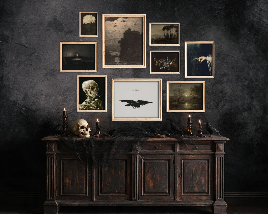 A gallery wall arrangement of framed gothic and horror art prints displayed above a dark wooden console table with candles, a skull, and black fabric, against a dark textured wall.