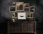 A gallery wall arrangement of framed gothic and horror art prints displayed above a dark wooden console table with candles, a skull, and black fabric, against a dark textured wall.