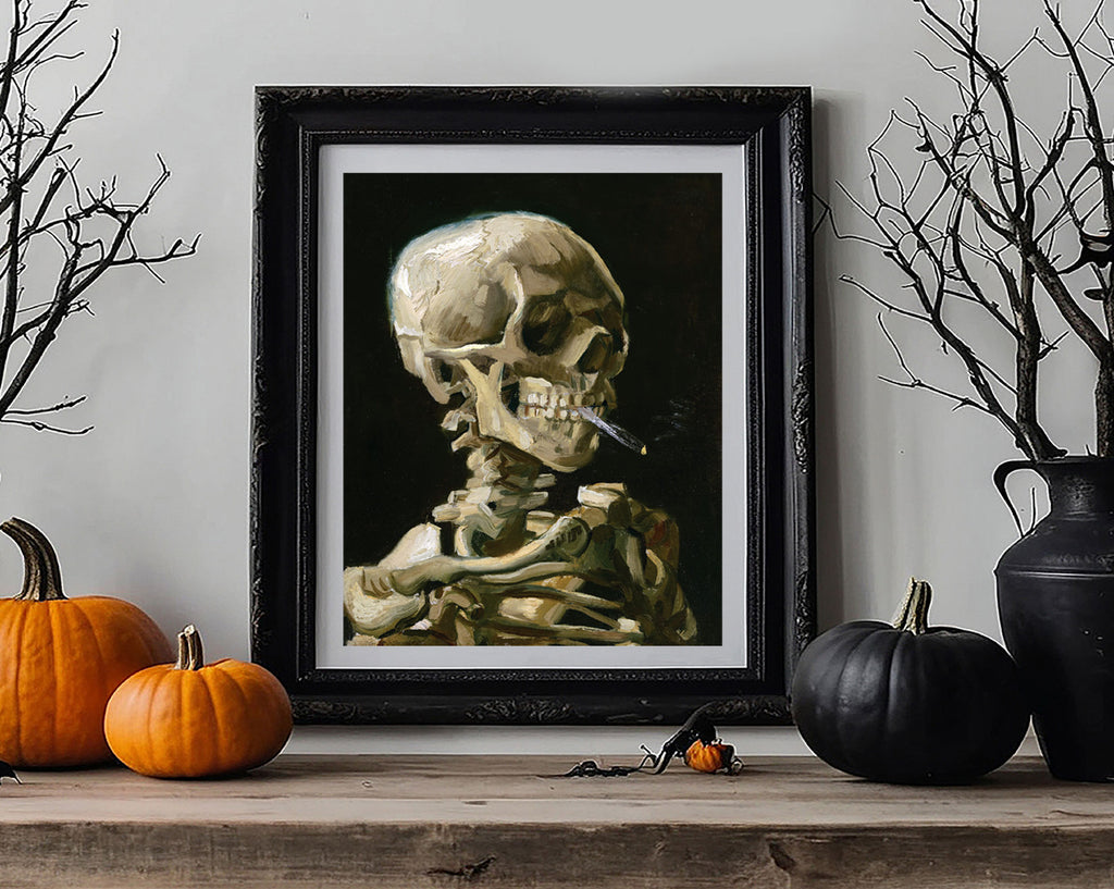 A framed art print depicting a detailed human skeleton smoking a cigarette, styled on a wooden mantel with pumpkins, bare branches, and a black vase against a light gray wall.
