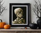 A framed art print depicting a detailed human skeleton smoking a cigarette, styled on a wooden mantel with pumpkins, bare branches, and a black vase against a light gray wall.