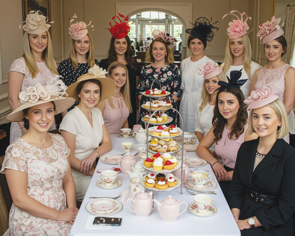 Group of women wearing festive hats at a formal event with a table of tea and pastries.